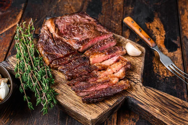 Pečené a nakrájené žebírko hovězí steak na dřevěné řezací desce s tymiánem. Tmavé dřevěné pozadí. Horní pohled — Stock fotografie