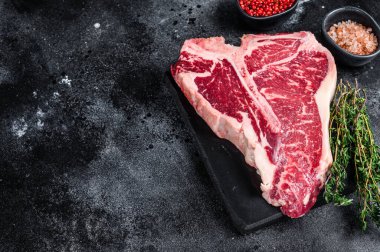 Kurumuş Raw T-bone ya da biftekli biftek, otlar ve tuzlu. Siyah arka plan. Üst Manzara. Boşluğu kopyala