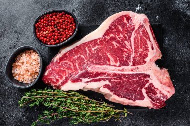 Kurumuş Raw T-bone ya da biftekli biftek, otlar ve tuzlu. Siyah arka plan. Üst görünüm