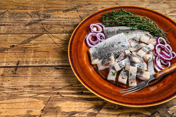 Filete cortado en rodajas de pescado de arenque marinado en escabeche en un plato con tomillo y cebolla. fondo de madera. Vista superior. Copiar espacio —  Fotos de Stock
