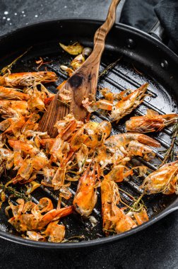 Arta kalan karidesler, tavada karidesler. Yiyecekler soyuldu, kafaların ayrıntıları verildi. Siyah arka plan. Üst görünüm