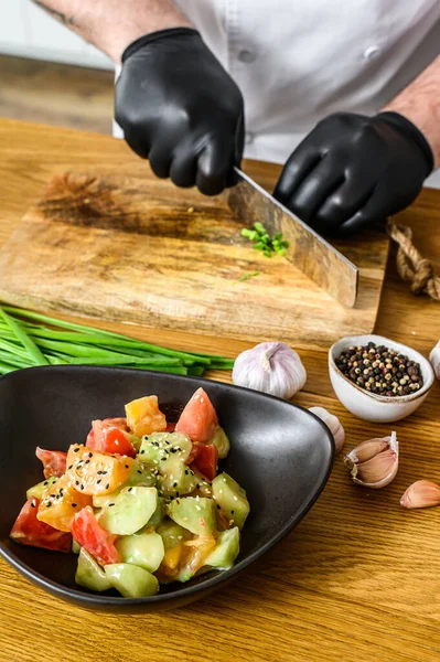 Um chef de luvas pretas está cortando cebolas verdes frescas em uma tábua de corte de madeira. Conceito de cozinhar alimentos orgânicos saudáveis — Fotografia de Stock