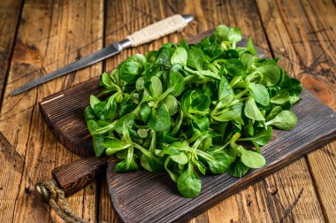 Tahta kesme tahtasının üzerinde taze çiğ yeşil kuzular marul mısır salatası yaprakları. Ahşap arka plan. Üst görünüm
