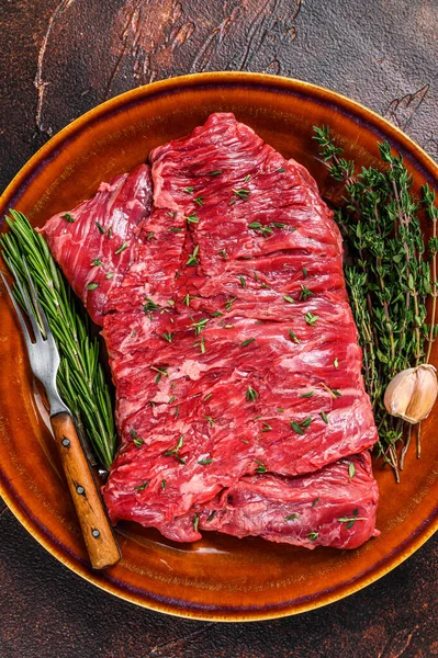 Raw beef skirt meat steak on a rustic plate with herbs. Dark background. Top view — Stock Photo, Image