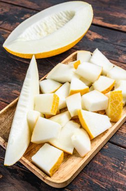 Tahta tepside dilimlenmiş sarı kavun küpleri. Koyu ahşap arka plan. Üst görünüm