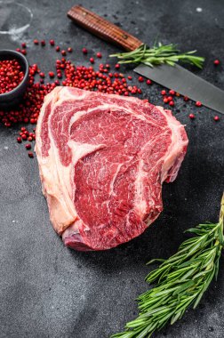 Çiğ kovboy bifteği ya da kemiğe otlar sürülmüş pirzola. Mermer biftek. Siyah arka plan. Üst görünüm.