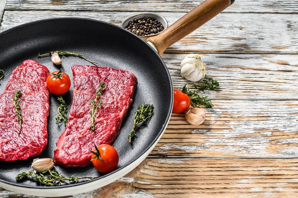 Bife de mármore bife Denver em uma panela com ervas. Carne orgânica. Fundo de madeira branco. Vista superior. Espaço de cópia — Fotografia de Stock