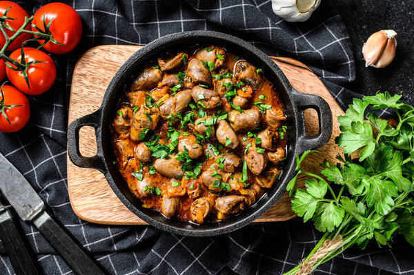 Stew with chicken hearts and vegetables with fresh parsley. Black background. Top view