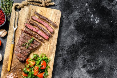 Kesme tahtasında baharatlı ızgara biftek. Mangal bifteği. Siyah arka plan. Üst Manzara. Boşluğu kopyala