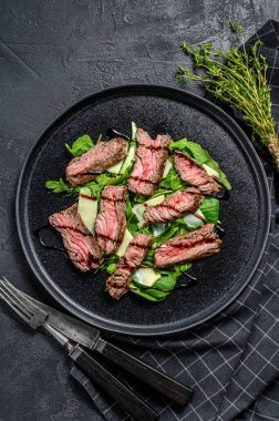 Ispanaklı biftek salatası, roka ve dilimlenmiş biftek. Siyah arka plan. Üst görünüm