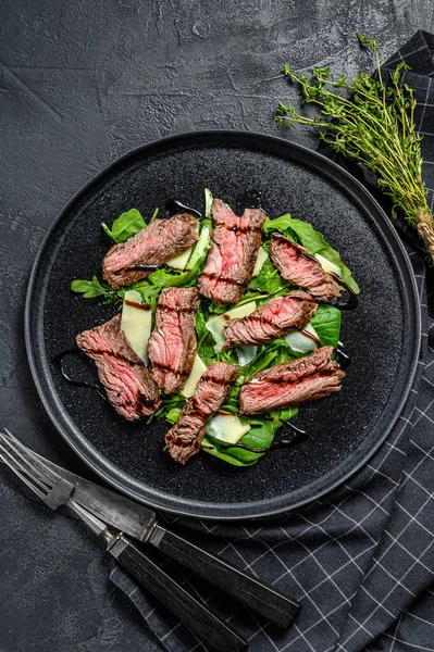 Steakový salát se špenátem, rukolou a nakrájeným hovězím steakem. Černé pozadí. Horní pohled — Stock fotografie
