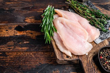 Çiğ kesilmiş tavuk göğsü fileto pirzolaları tahta bir kesme tahtasının üzerinde satırla. Koyu ahşap arka plan. Üst Manzara. Boşluğu kopyala