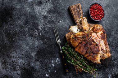 Ahşap bir tahtanın üzerinde kızarmış domuz budu ve şifalı otlar. Siyah arka plan. Üst Manzara. Boşluğu kopyala