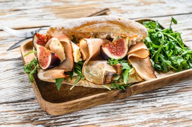 Arugula, incir, prosciutto, Ciabatta ve ahşap tepside mavi peynirli sandviç. Beyaz arka plan. Üst görünüm