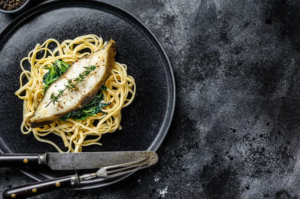 Baked Halibut fish steak and Spaghetti pasta with spinach. Black background. Top view. Copy space