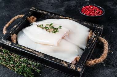 Ahşap tepside otlu çiğ beyaz mürekkep balığı ya da kalamar. Siyah arka plan. Üst görünüm