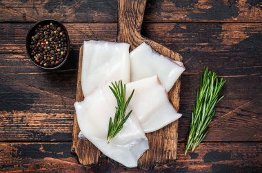 Ahşap bir tahtada biberiyeli çiğ kalamar ya da mürekkep balığı. Koyu ahşap arka plan. Üst görünüm