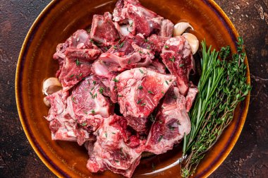 Gulaş için kesilmiş çiğ koyun eti ya da kırsal bir tabakta kemikli güveç. Karanlık arka plan. Üst görünüm