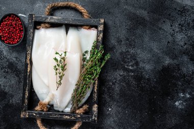 Ahşap tepside otlu çiğ beyaz mürekkep balığı ya da kalamar. Siyah arka plan. Üst Manzara. Boşluğu kopyala