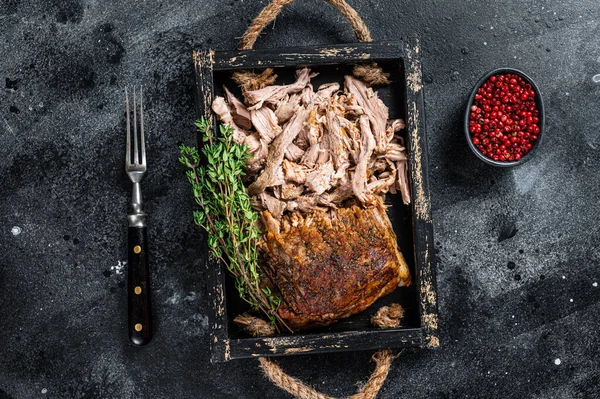 Bbq slow roast puilled pork meat in a wooden tray. Black background. Top view