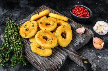 Kesme tahtasının üzerinde kızartılmış kalamar halkaları. Siyah arka plan. Üst görünüm