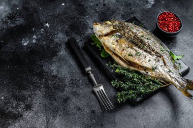 Kesme tahtasında otlu kavrulmuş balık. Siyah arka plan. Üst Manzara. Boşluğu kopyala