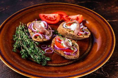 Zeytinyağı, otlar, domatesler ve baharatlı ançüezli fileto ekmekli İspanyol tapaları. Karanlık arka plan. Üst görünüm