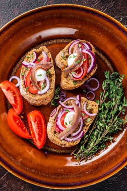 Zeytinyağı, otlar, domatesler ve baharatlı ançüezli fileto ekmekli İspanyol tapaları. Karanlık arka plan. Üst görünüm