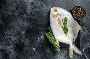 Mermer bir tahtanın üzerinde otlu çiğ balık ponponu. Siyah arka plan. Üst Manzara. Boşluğu kopyala