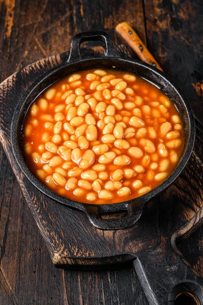 Beans in tomato sauce in a pan. Dark wooden background. top view.