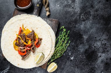 Meksika Fajitası, renkli biber ve soğanlı, tortilla ve salsa ile servis ediliyor. Siyah arka plan. Üst Manzara. Boşluğu kopyala.