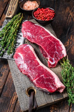 Tahta kesme tahtasının üzerinde çiğ sığır filetosu bifteği ve otlar. Koyu ahşap arka plan. Üst görünüm.