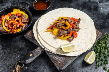 Meksika Fajitası, renkli biber ve soğanlı, tortilla ve salsa ile servis ediliyor. Siyah arka plan. Üst görünüm.