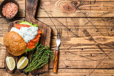 Tuzlu balık somonlu sandviç, avokado, hamburger ekmeği, hardal sosu ve buzdağı salatası. Ahşap arka plan. Üst Manzara. Boşluğu kopyala.