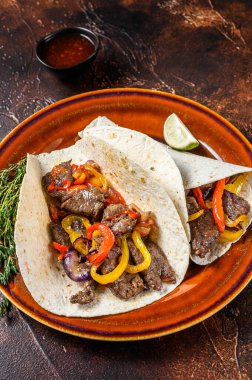 Fajitas Tortilla biftek şeritleri, tatlı biber ve soğanla sarılır. Karanlık ahşap arka plan. Üst görünüm.