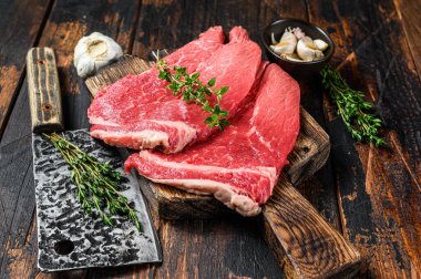 Kesme tahtasının üzerinde çiğ et, pirzola ve biftek. Koyu ahşap arka plan. Üst görünüm.