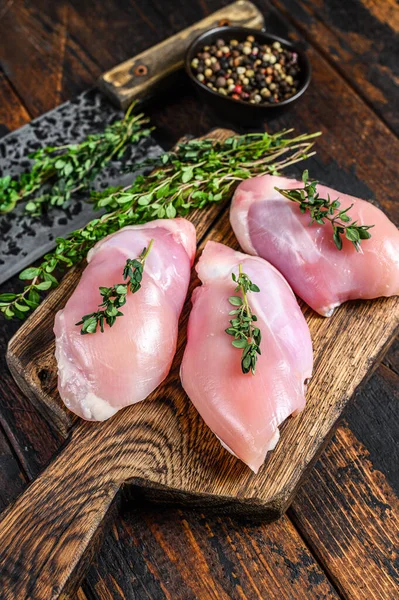 Raw Chicken skinless thigh fillet on a wooden cutting board. Black background. Top view.