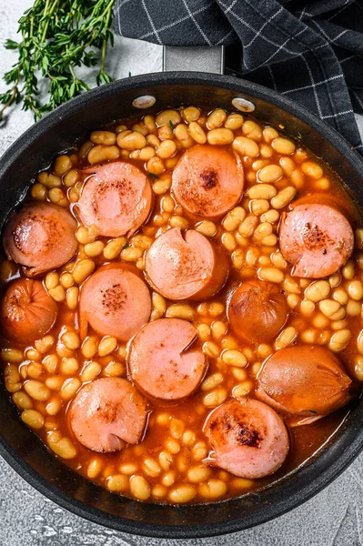 Beans with sausages in tomato sauce in a pan. White background. Top view.