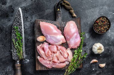 Tahta bir kesme tahtasının üzerinde dilimlenmiş çiğ tavuk filetosu. Siyah arka plan. Üst görünüm.
