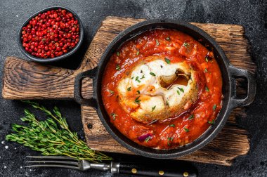 Tavada domatesli haşlanmış beyaz balık. Siyah arka plan. Üst görünüm.