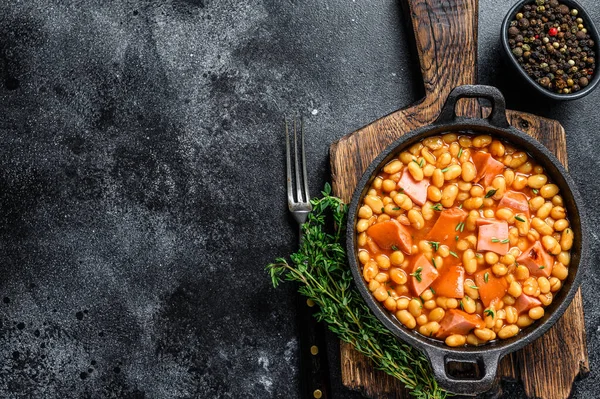 Stewed Kidney beans with smoked sausage and tomato sauce in a pan. Black background. Top view. Copy space.