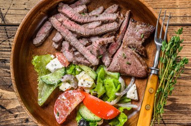 Ahşap tabakta biftek ve sebze salatası ile sığır eti pirzolası. Ahşap arka plan. Üst görünüm.