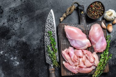 Tahta bir kesme tahtasının üzerinde dilimlenmiş çiğ tavuk filetosu. Siyah arka plan. Üst Manzara. Boşluğu kopyala.