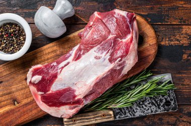 Tahta bir kasapta çiğ kuzu eti ya da keçi omuzu eti, satırla tahtayı keser. Koyu ahşap arka plan. Üst görünüm