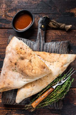 Ev yapımı Calzone, ahşap tahtada jambon ve peynirli kapalı pizza. Koyu ahşap arka plan. Üst görünüm