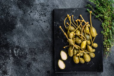 Mermer bir tahtanın üzerinde turşulu kapari. Siyah arka plan. Üst Manzara. Boşluğu kopyala