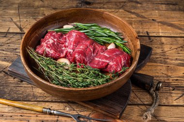 Tahta tabakta çiğ, etekli biftek ve şifalı otlar. Ahşap arka plan. Üst görünüm