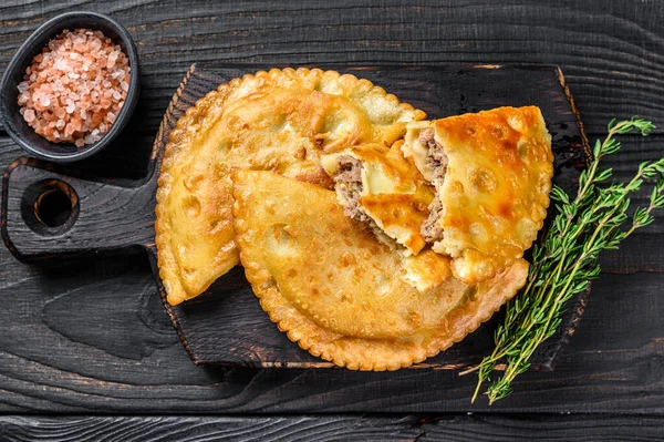 Cheburek etli börek ve şifalı otlar. Siyah ahşap arka plan. Üst görünüm