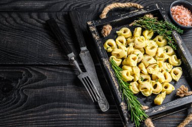 Tahta tepside ıspanaklı İtalyan geleneksel tortellini makarnası. Siyah ahşap arka plan. Üst Manzara. Boşluğu kopyala