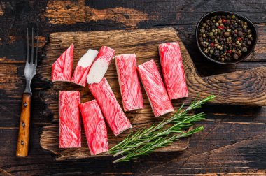Tahta kesme tahtasına dilimlenmiş yengeç surimi çubukları. Koyu ahşap arka plan. Üst görünüm